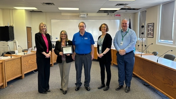 image of five individuals posing for office photo with one of them holding a certificate for camera to view.
