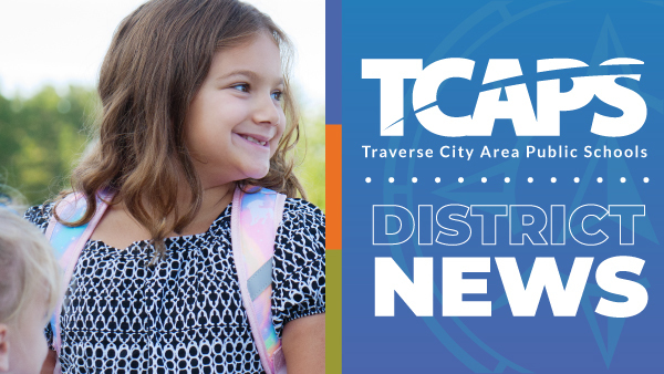  A young, smiling elementary-aged girl with a backpack looks to the right side of the frame. The right side of the image features the Traverse City Area Public Schools (TCAPS) logo and the words "District News" on a blue and orange background.