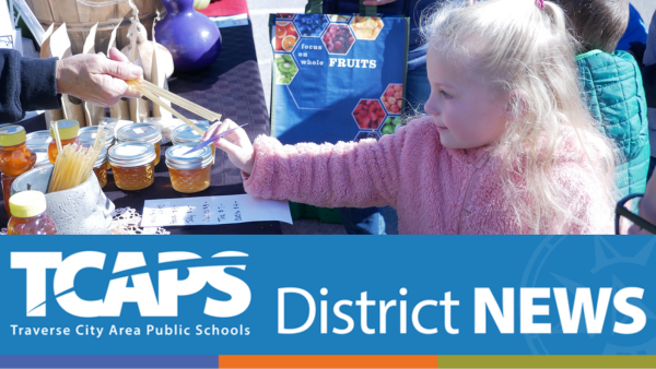 image of little girl wearing pink coat standing at farmers market table with honey.