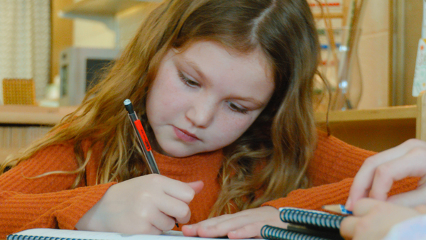 young girl writing on paper with mechanical pencil.