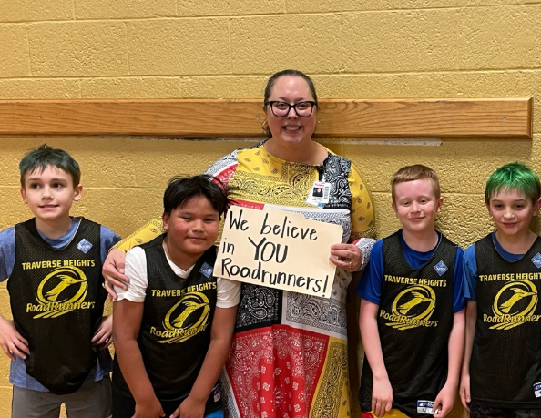 teacher standing with students in hallway holding sign that reads "we believe in you roadrunners"