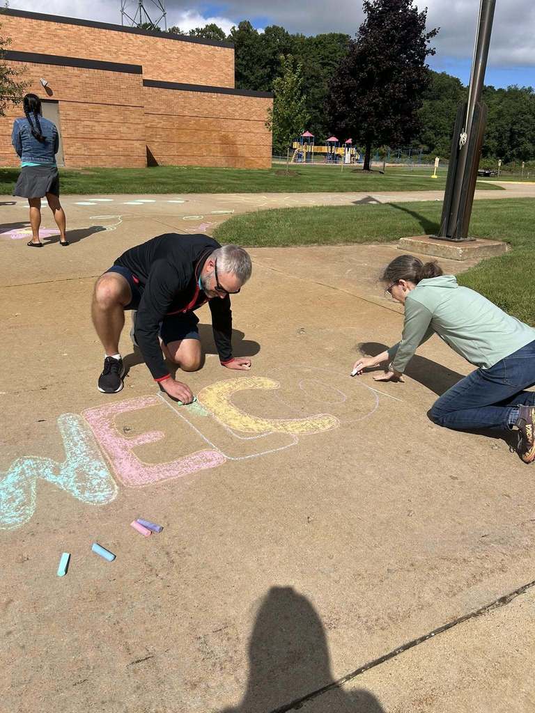TCAPS staff writing the word welcome in chalk outside the school
