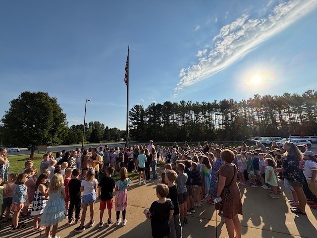 Staff members and students standing in front of a flag outside  the school