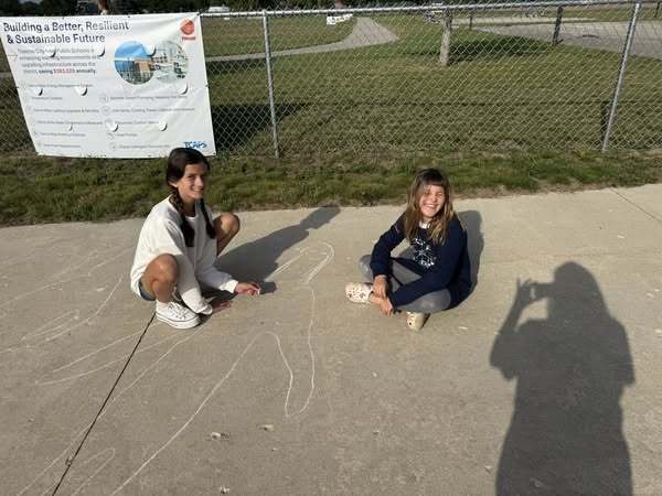 students  chalk drawing outside on the school cement