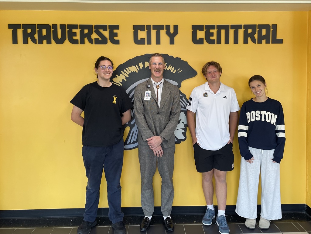 Principal and three students standing in front of a wall in the school hallway