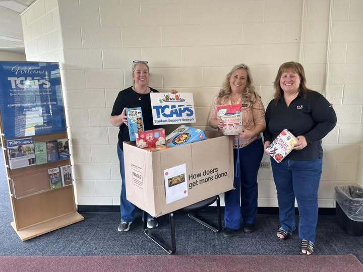 Chelsea Park West employees and Student Support Network's Katie Kubesh standing behind box of school supplies