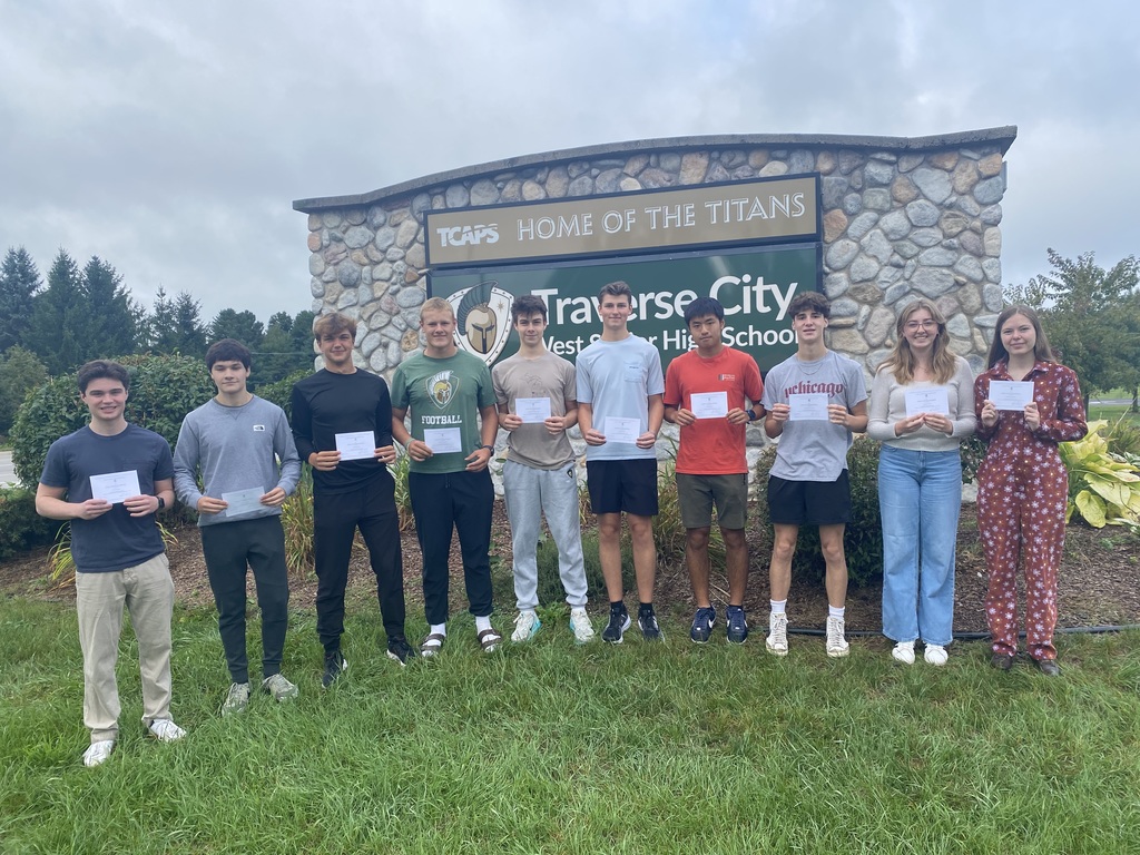 students standing outside in front of school sign