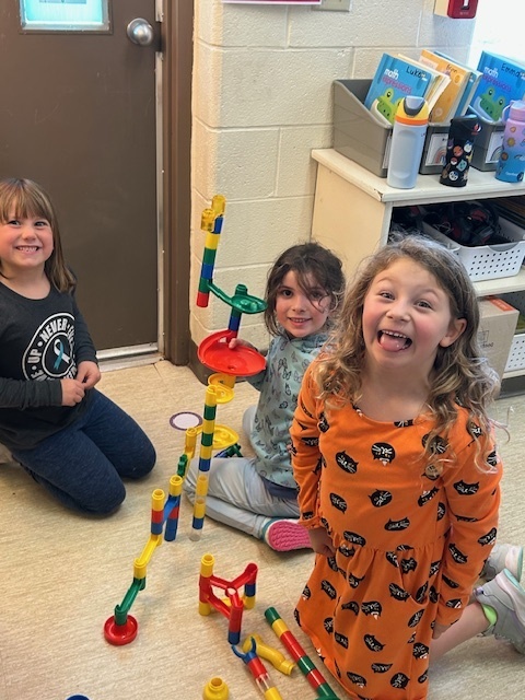 3 students buiding a marble run and smiling