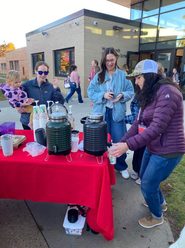 3 parents standing around a table with a red table cloth getting coffee