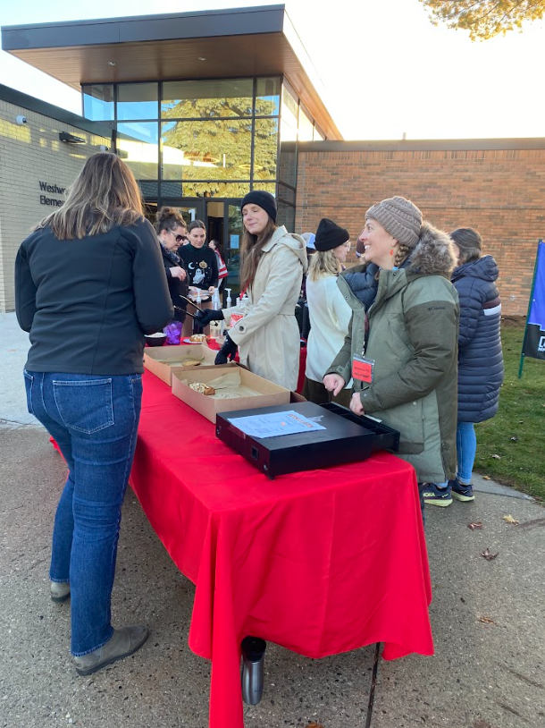 adults standing in front of a red table buying pastries and talking