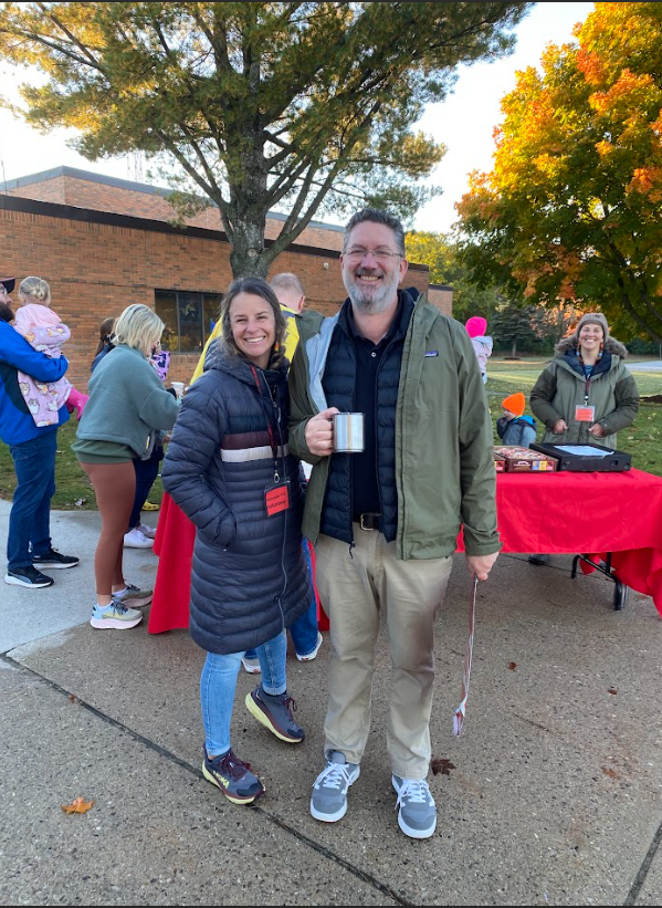 PTO President Crystal DeCora and Westwoods Principal Toby Tisdale  standing in front of a coffee and pastry table with a red tablecloth, one adult holding a cup of coffee