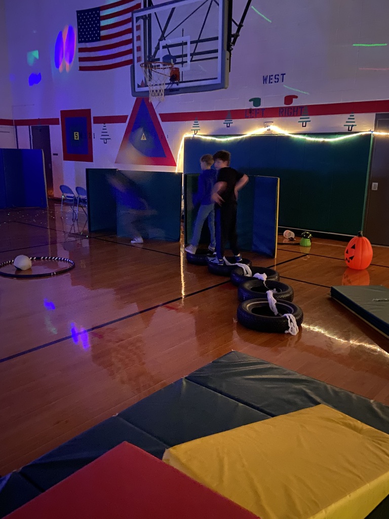 Two male students going through an obstacle course, with tires and tumbling mats.