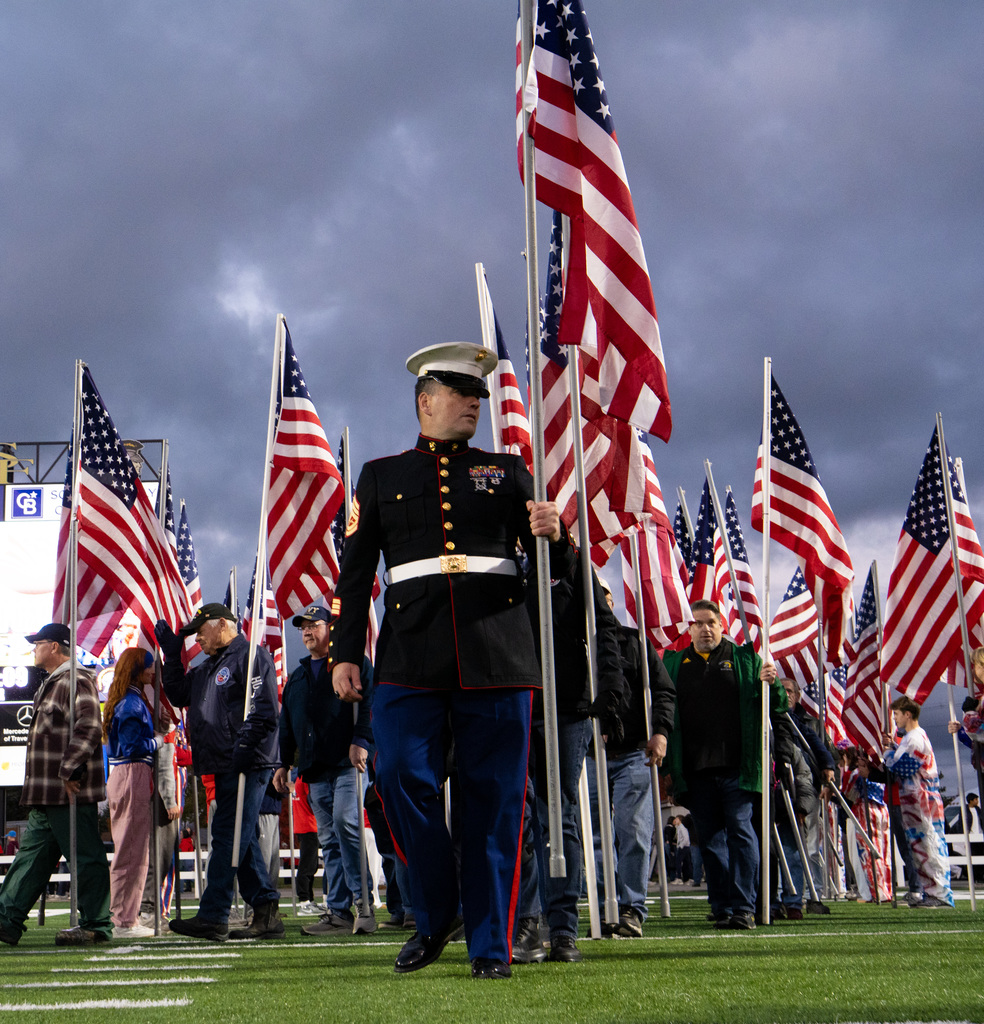 Several Veterans, first responders, active-duty military, and area heroes holding American flag before kickoff on football field