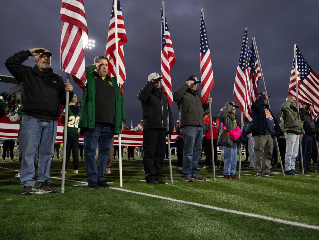 Several Veterans, first responders, active-duty military, and area heroes holding American flag before kickoff on football field