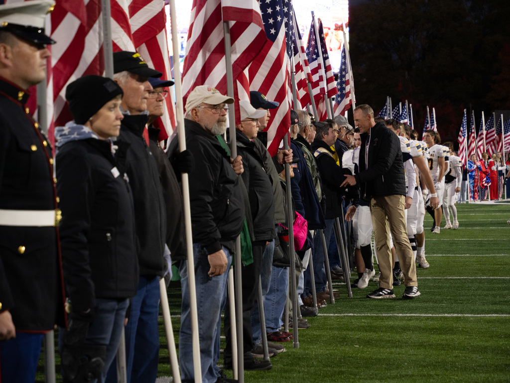 Several Veterans, first responders, active-duty military, and area heroes  holding American flag before kickoff on football field