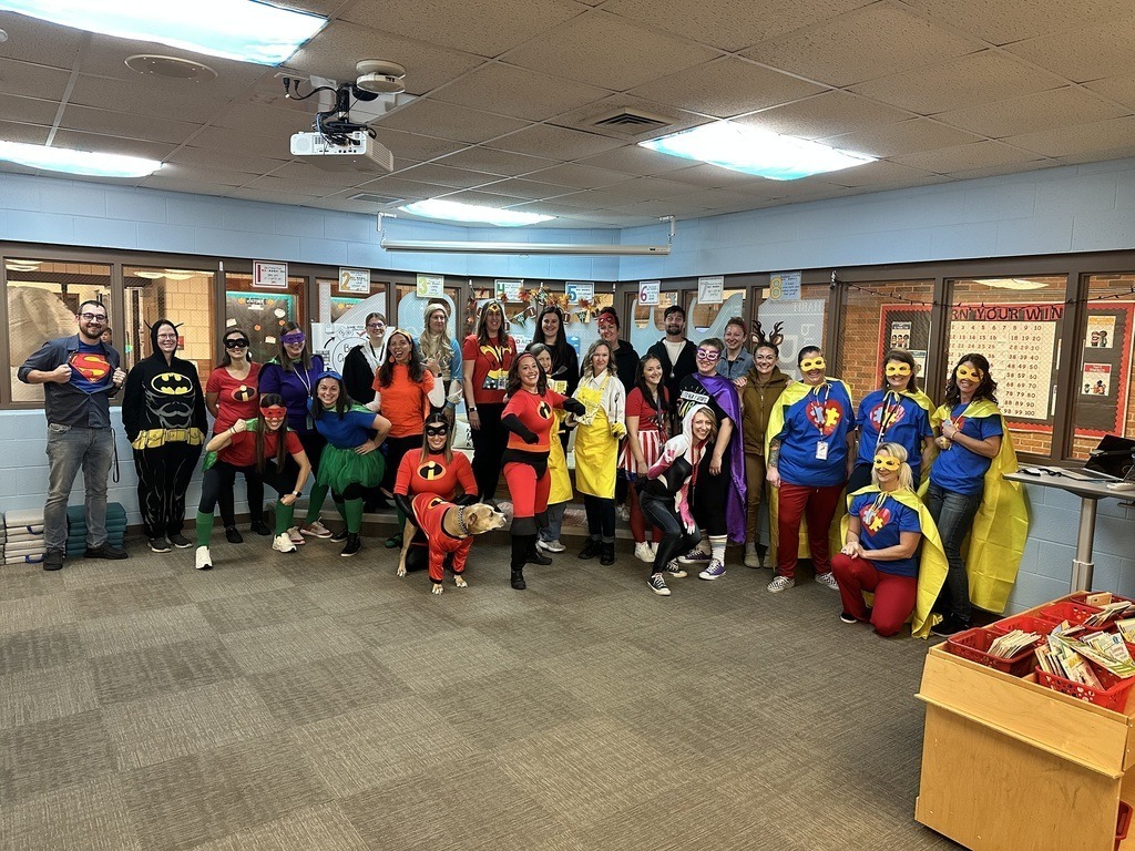 Westwoods Elementary staff dressed in a variety of colorful superhero and comic book costumes in a classroom.
