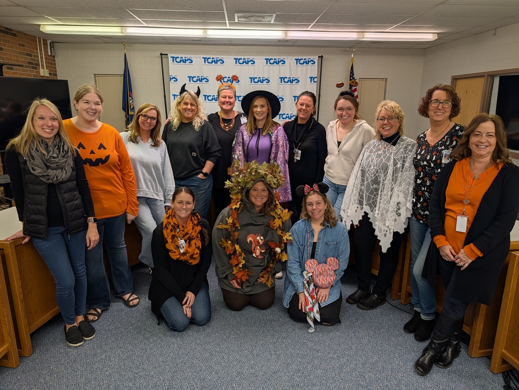 Staff members in costumes celebrating Halloween in a conference room with a TCAPS logo banner.