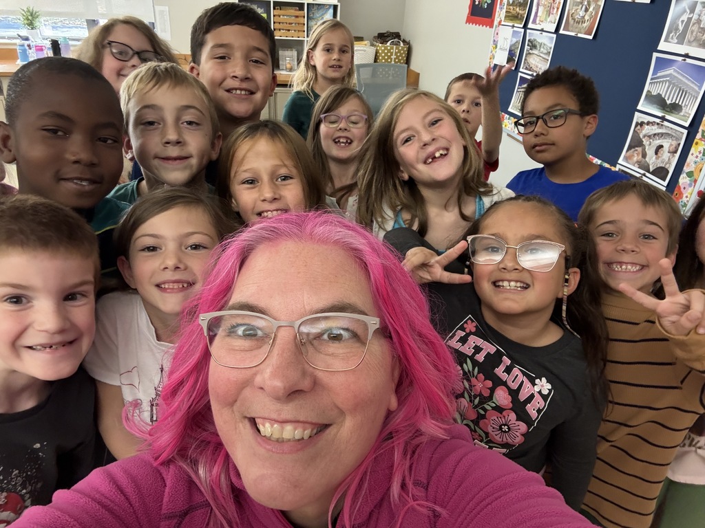 Pink haired principal  with students surrounding her in the classroom