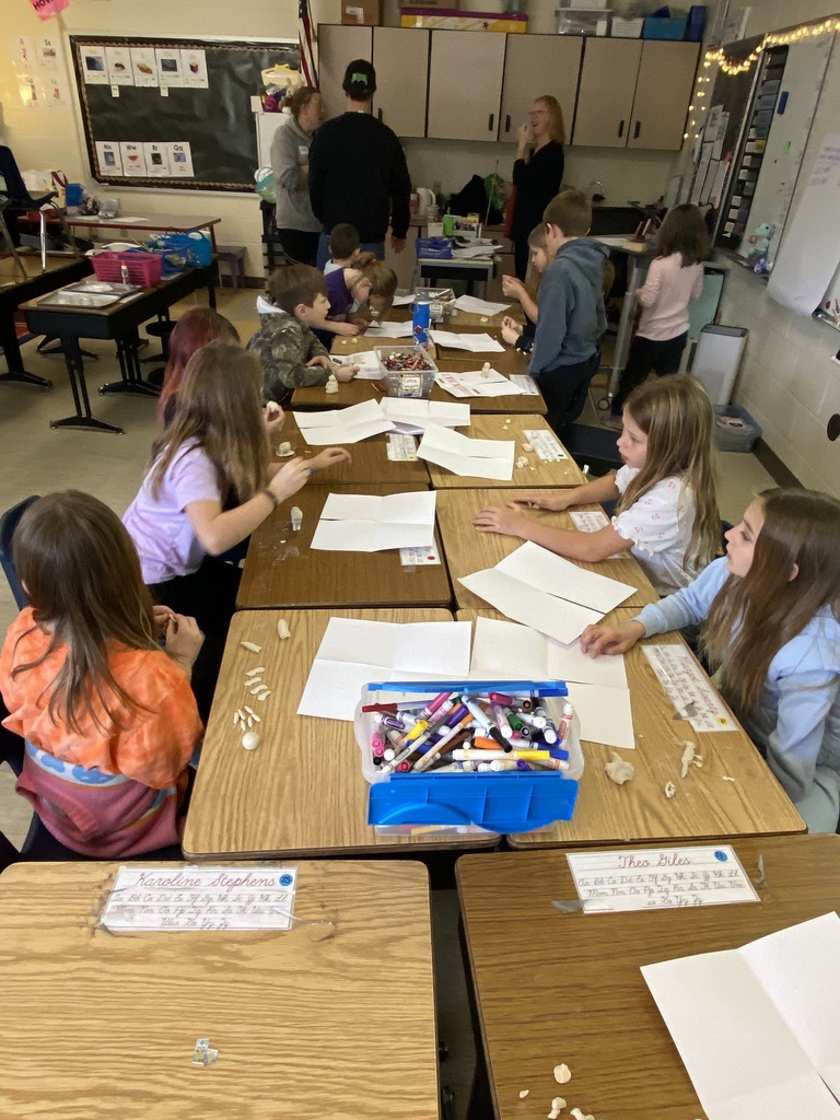 students sitting on a together, all of the desks are pushed together into a long line,  working on animal drawings
