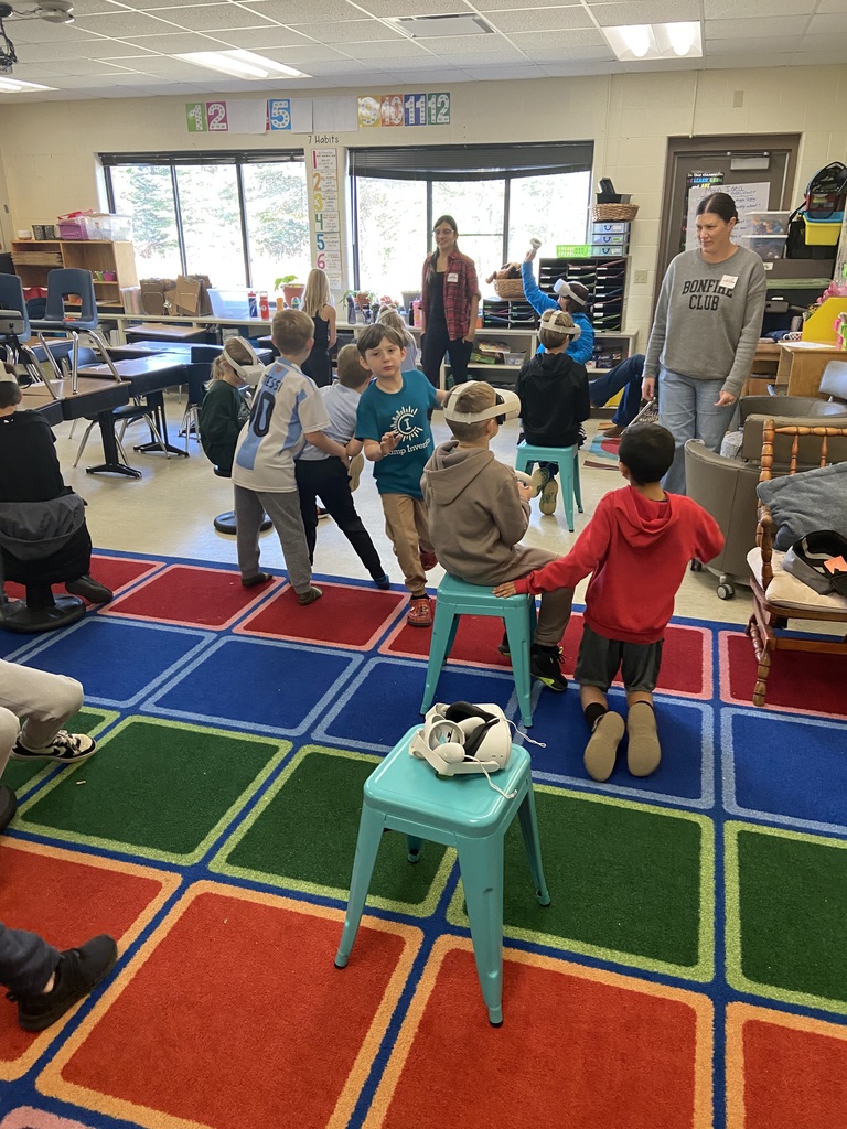 Student in a classroom sitting on  teal stools using VR headset