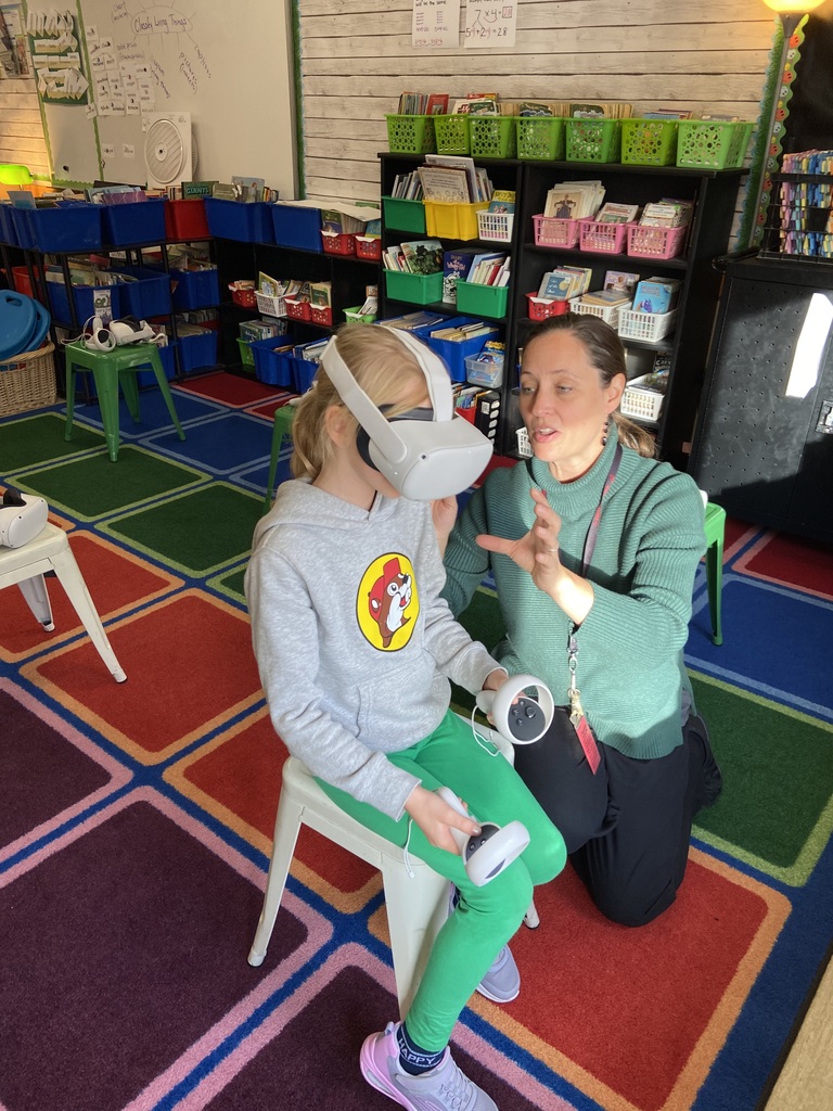 Mrs. Jackson helping a student who is sitting on a white stool using a VR headset.