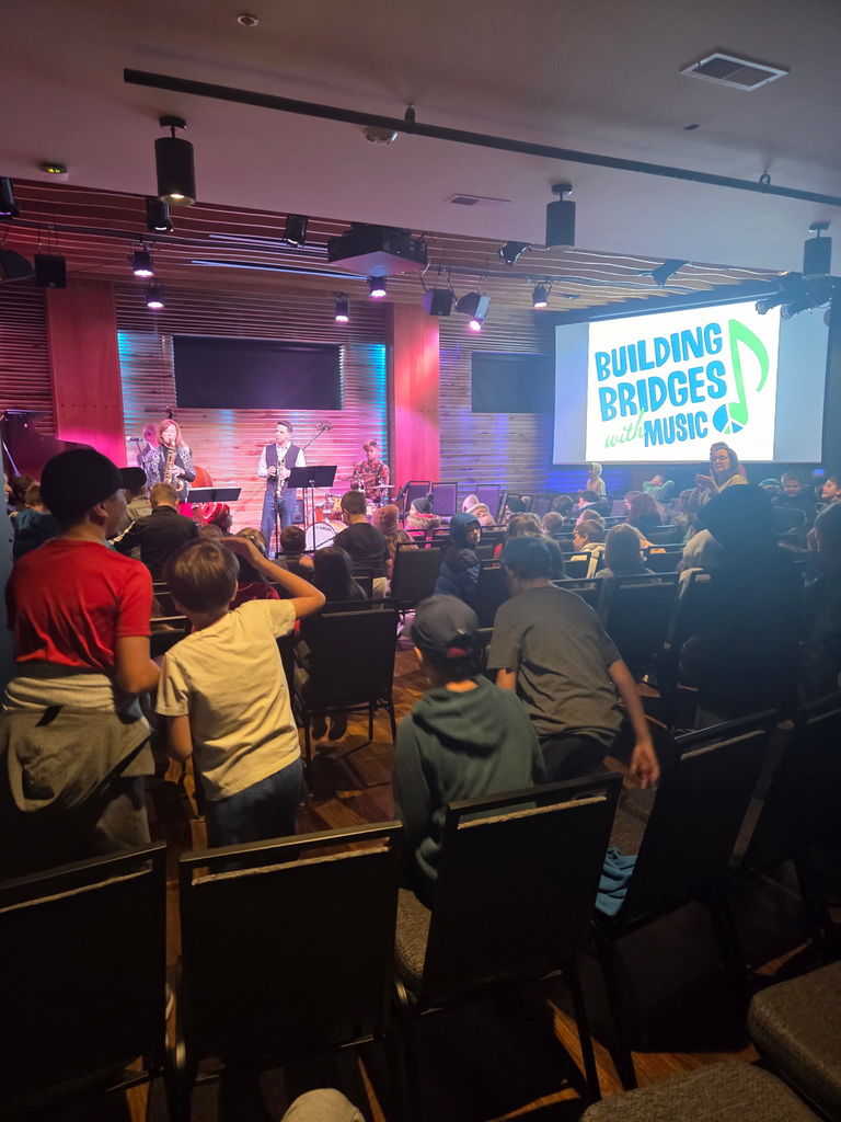 students listening to a band perform on stage, with a screen that says: building bridges with music