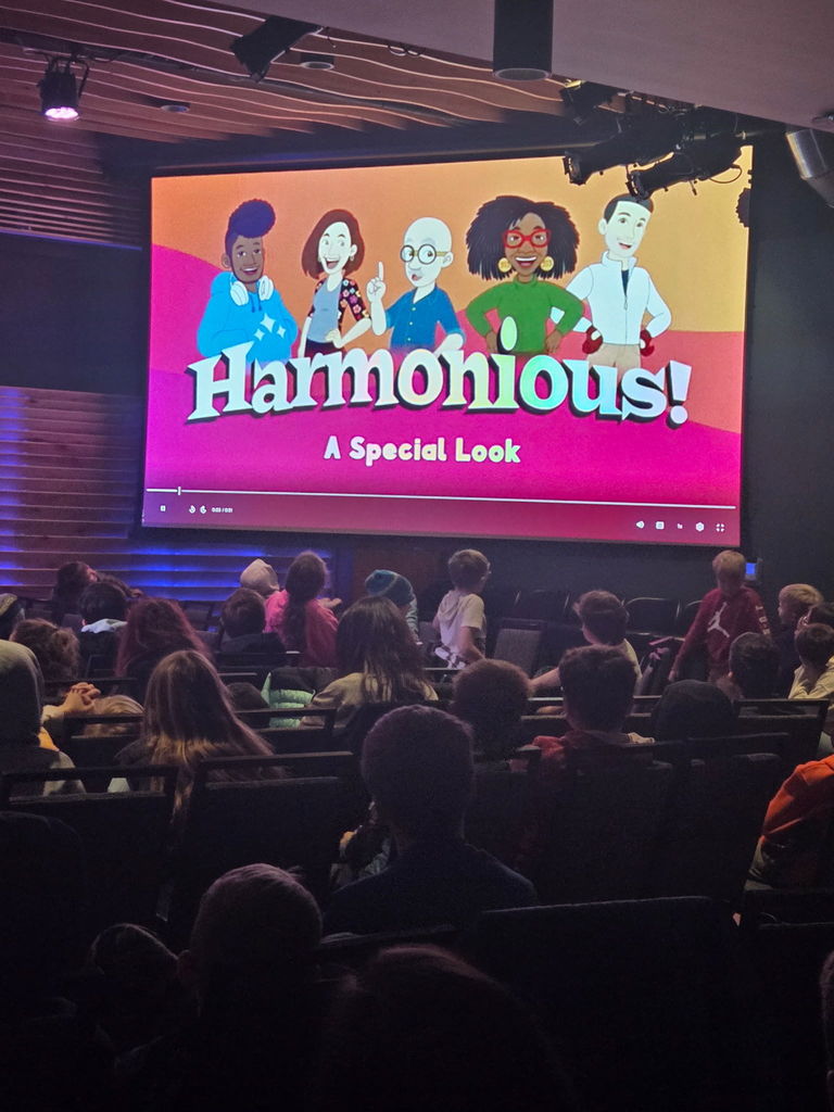 a sign reading  Harmonious! A special look with students sitting in seats looking at the sign