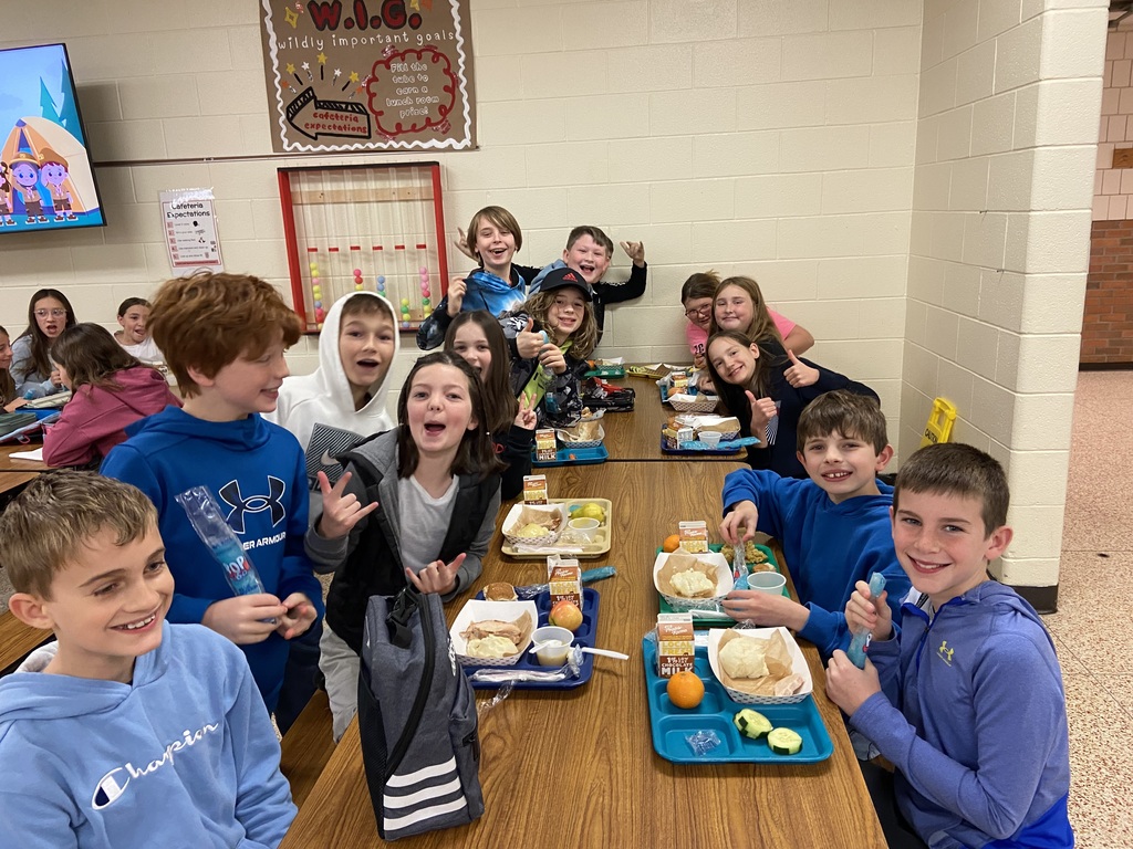 students sitting at a table eating, smiling and hands up