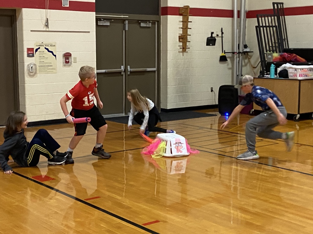 one student guarding the laundry basket with a pool noodle, while two other students try to grab the scarfs