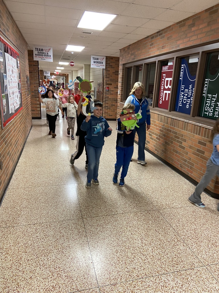 students walking down a hallway holding up paper plates decorated like balloons with their teacher