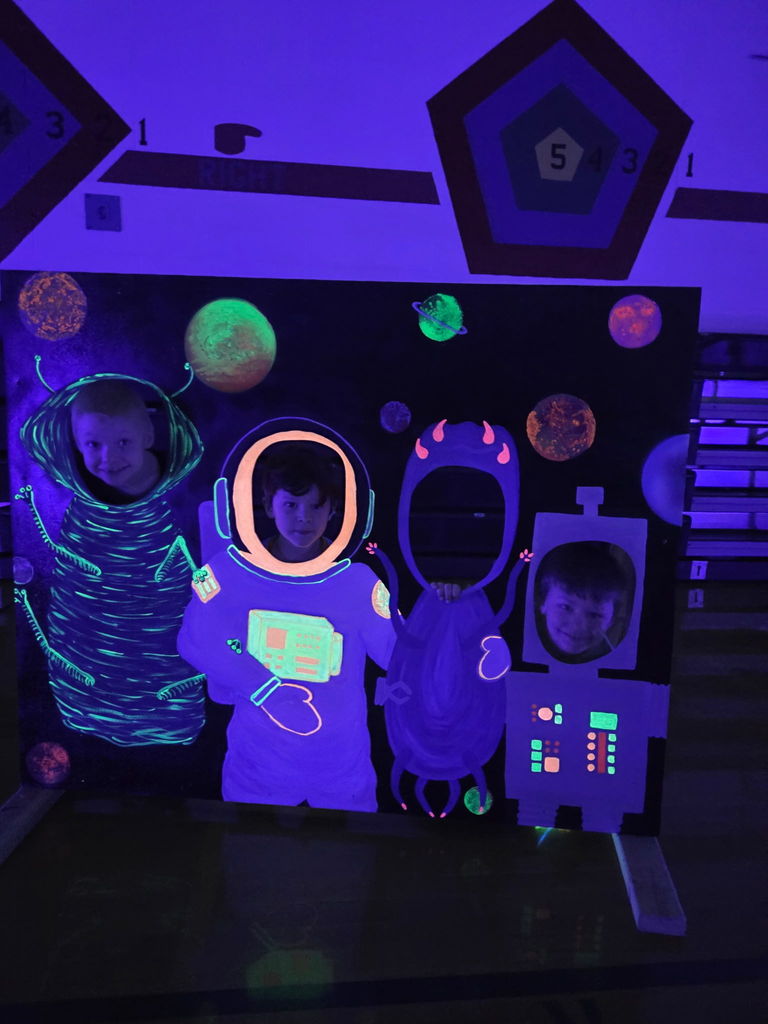 students putting their heads through a cutout of aliens that glow in the dark, students are smiling