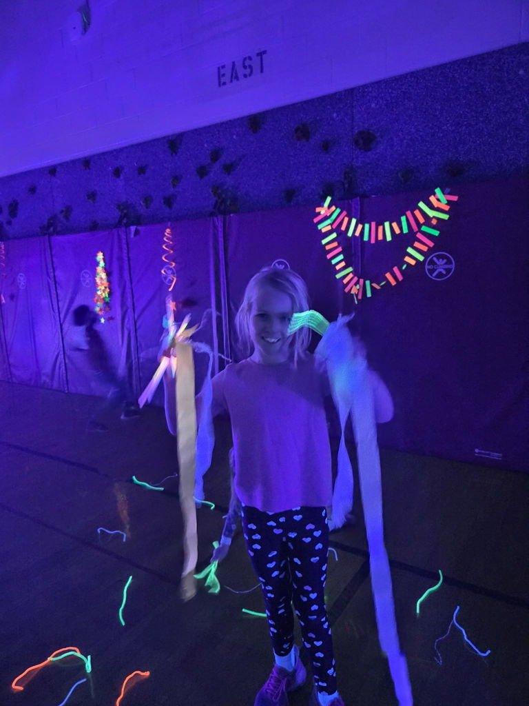 student standing in a dark gym holding glow sticks and smiling at the camera