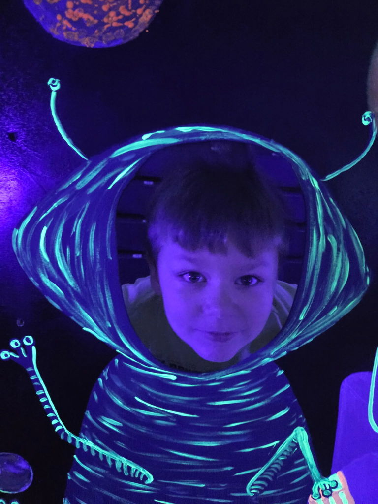 student putting his head an alien cut out that is glow in the dark smiling