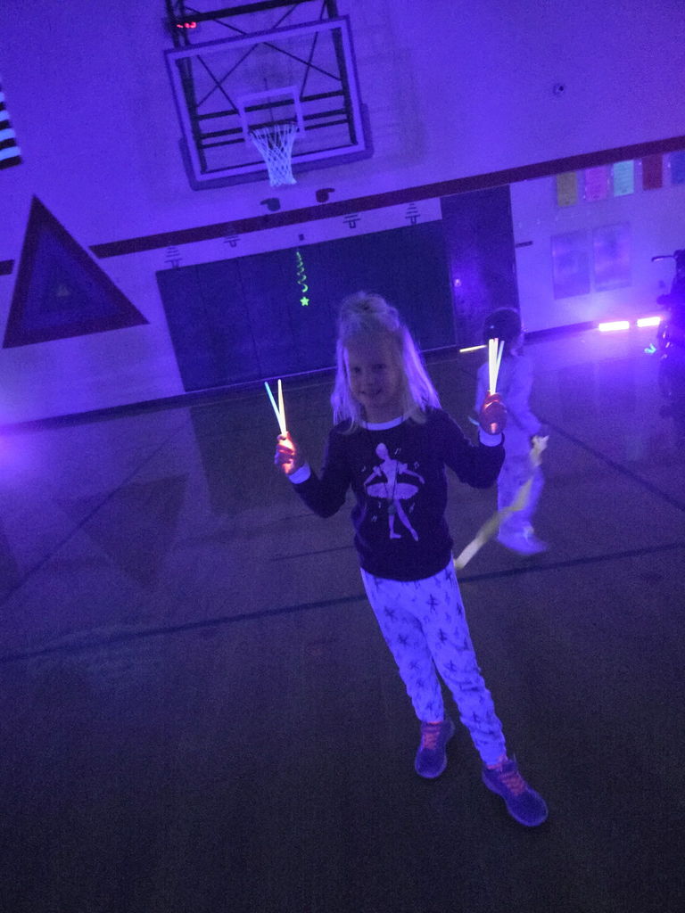 Student smiling  for the camera in a dark gym, holding glow sticks