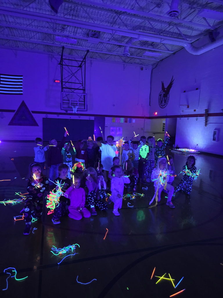 a class of students posing for the camera with glow sticks in their hand and on them, in a dark gym