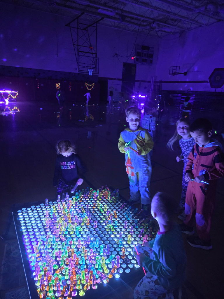 students standing over a glow table smiling and looking at it.
