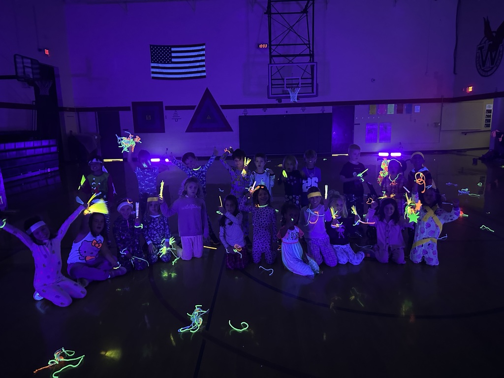 students smiling at the camera, posing for a class picture in dark gym with glowsticks