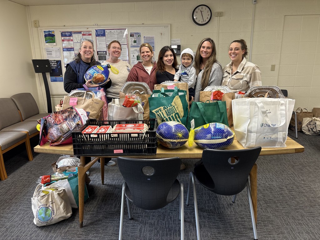 Six people and a child standing behind a table filled with Thanksgiving food donations including turkeys and grocery bags.