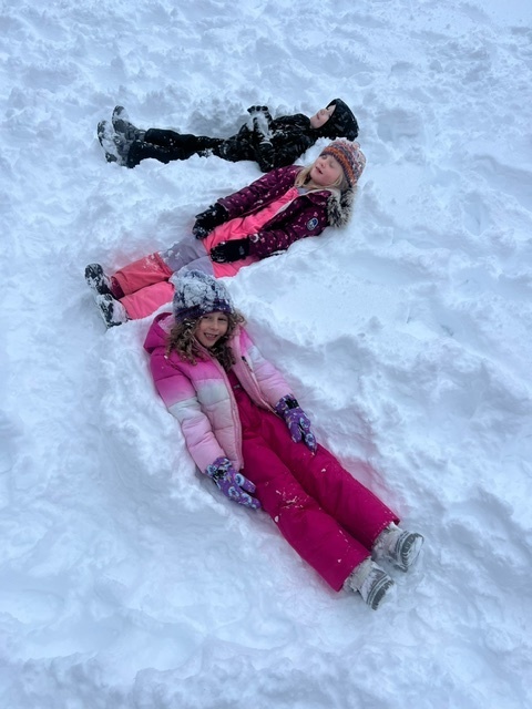 students laying in the snow in a zig zag pattern smiling at the camera