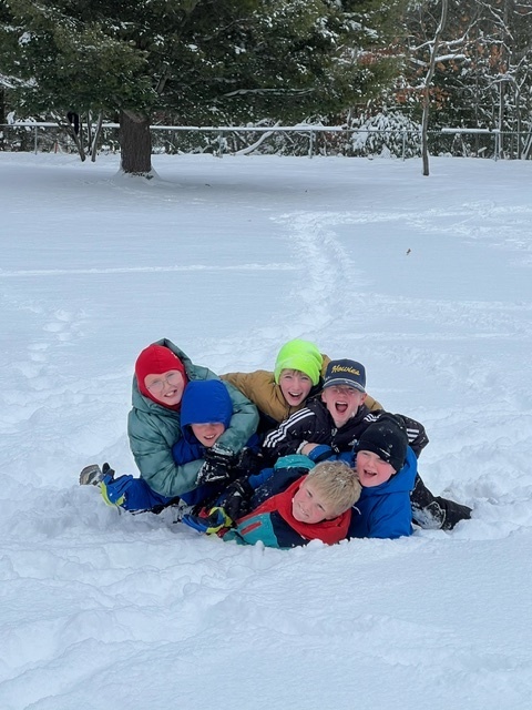 students outside in the snow piled ontop of each other smiling at the camera