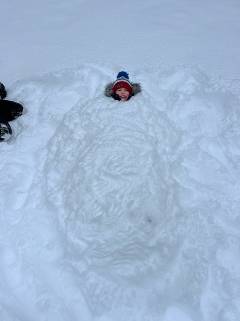 student buried in snow up to his neck smiling at the camera