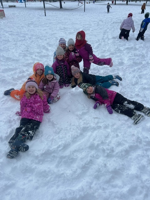 students sitting in snow in a triangle form smiling at the camera