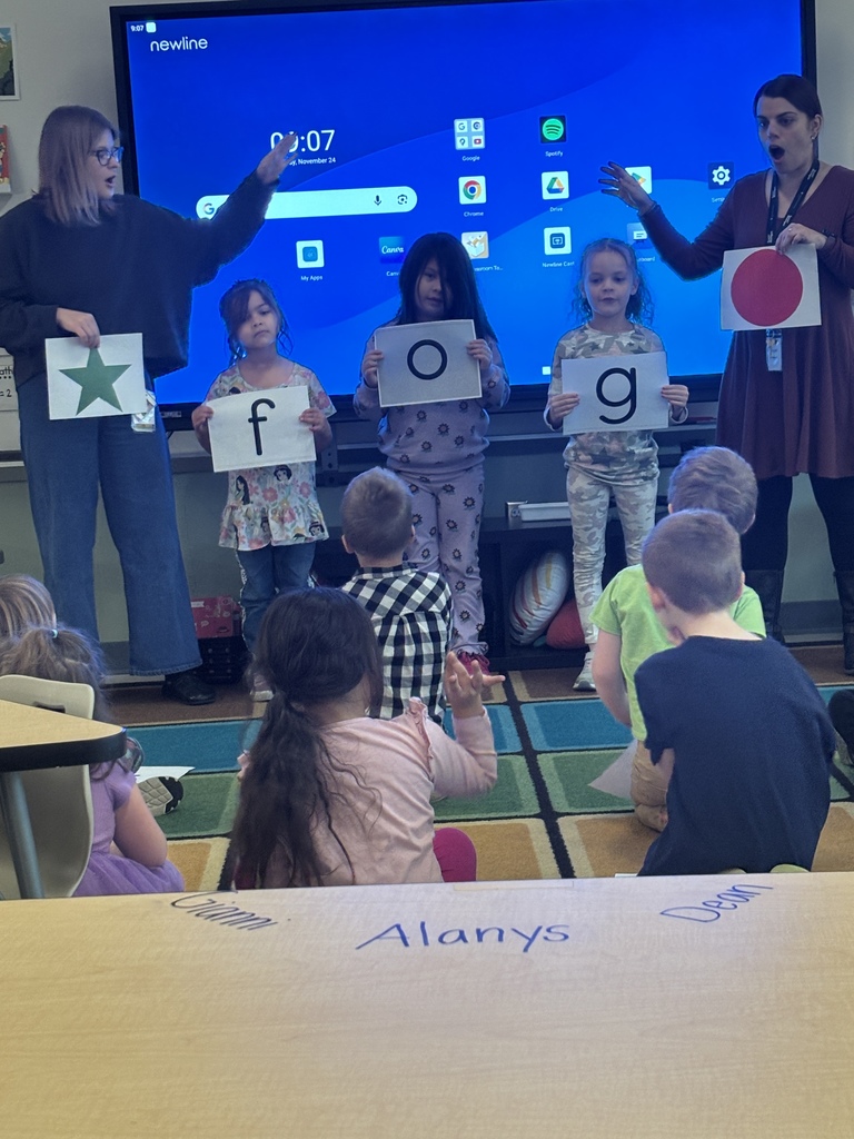 Teachers and students in a classroom hold up cards with shapes (star, circle) and letters ('f', 'o', 'g') for a lesson.