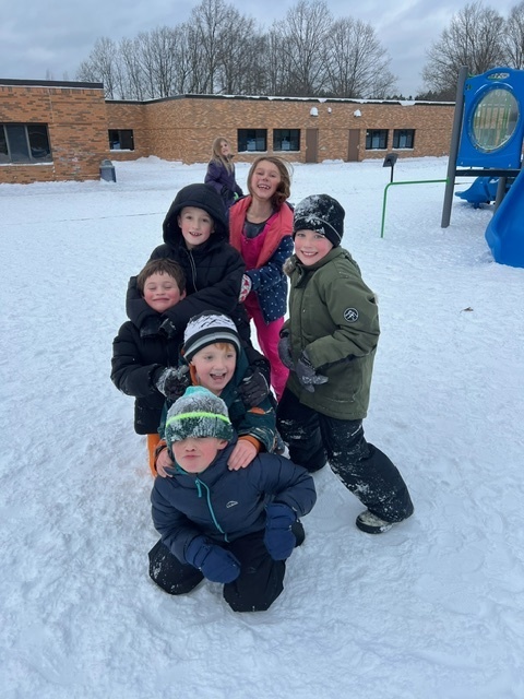 students smiling at the camera outside on the playground in the snow