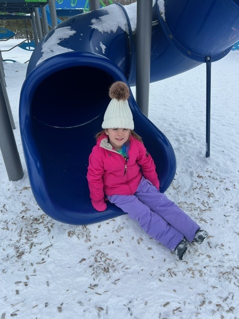student in snow gear sitting on the end of the slide