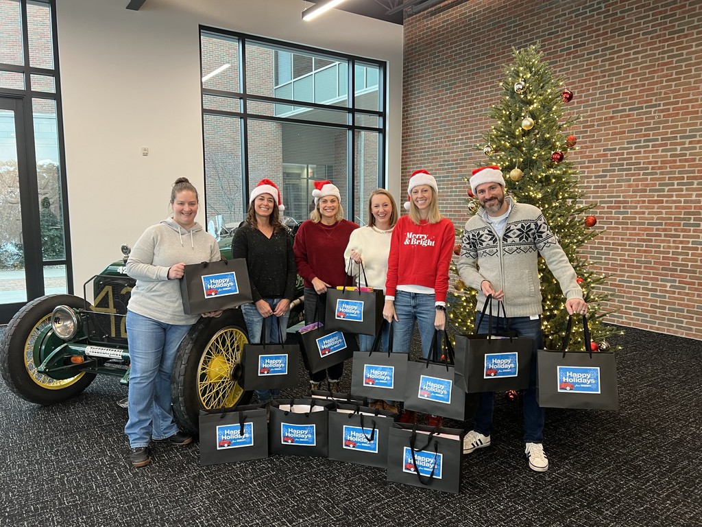 Hagerty Staff holding gift bags for tcaps students in front of tree and car.