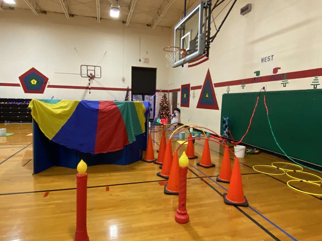 Christmas obstacle course: tall fake candles, cones with a hoop connecting them to walk through, a Christmas tree in the back 