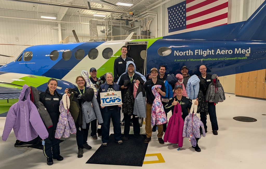 Staff from North Flight Aero Med and TCAPS Student Support Network smiling with winter gear donation. Airplane in the background.