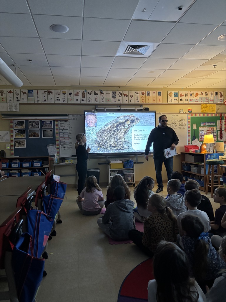 Teacher and student standing at the front of the room while students are sitting on the floor listening