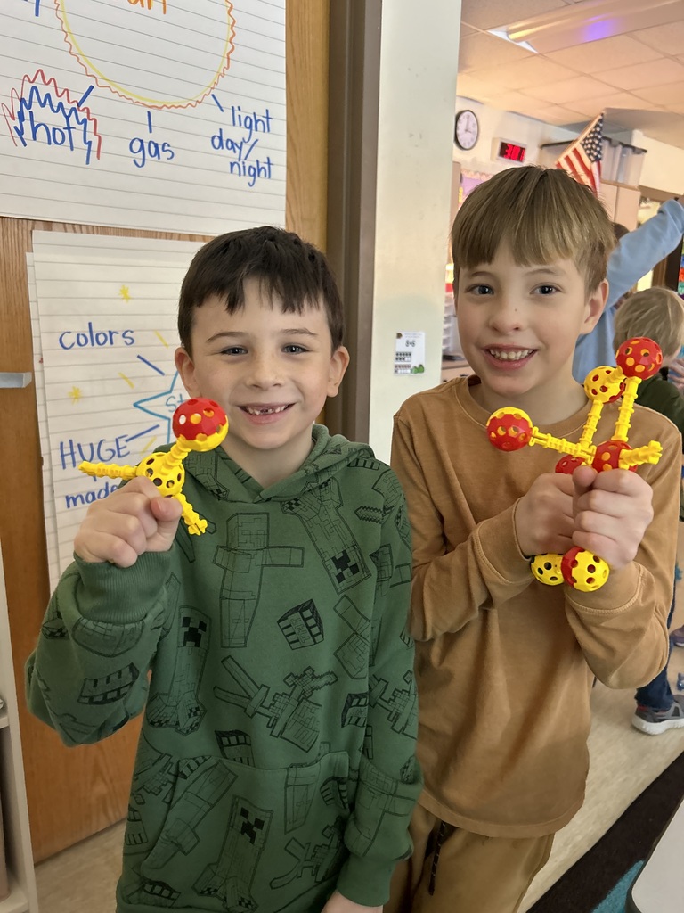 two students holding connecting yellow blocks with red balls on them 
